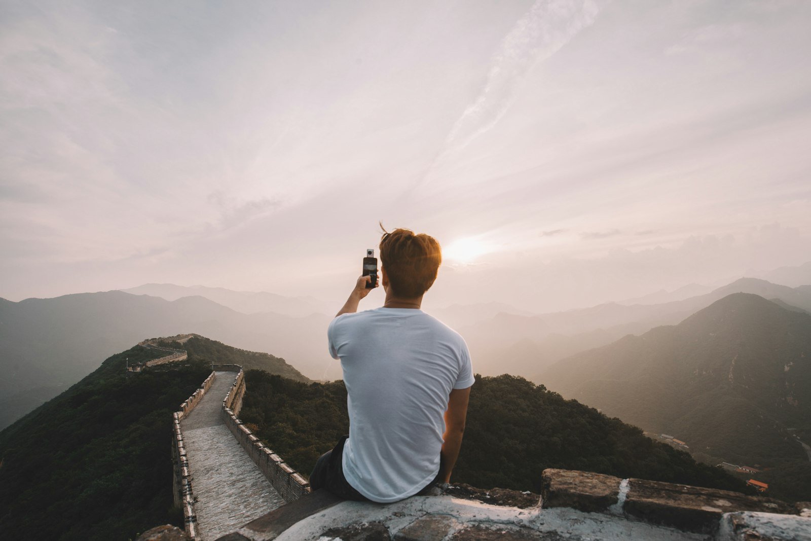 Person sitting on a cliff facing mountains, a remote spot with no cell signal